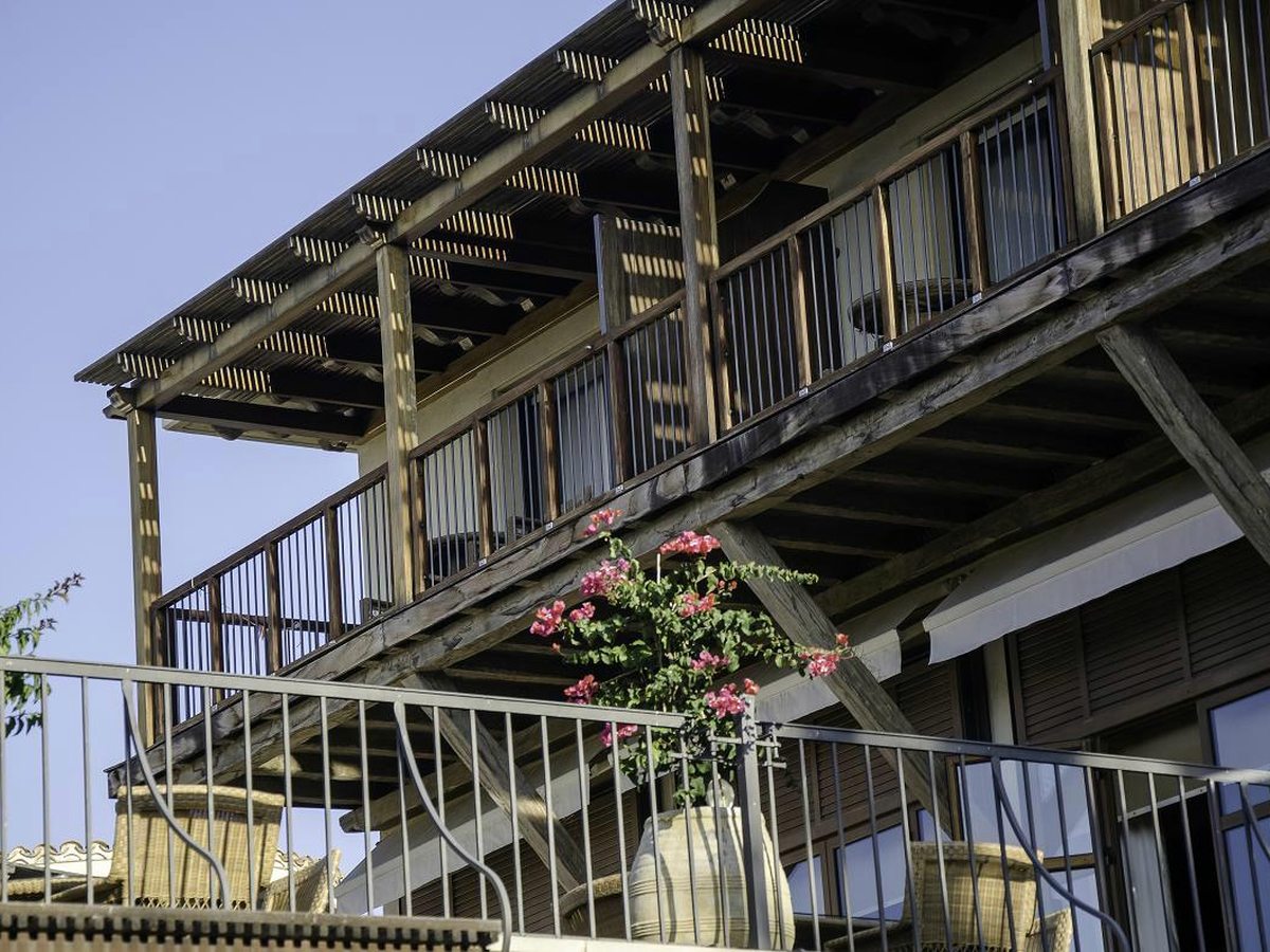 A whitewashed accommodation block with wooden balconies, pergola shades and bougainvillea.