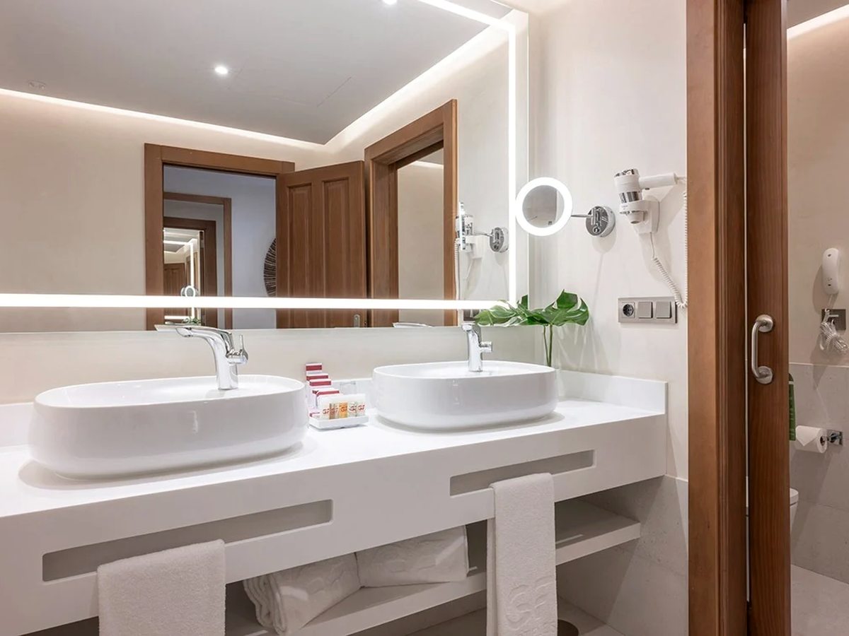 A refurbished bathroom with a long white vanity, two countertop basins and a large backlit mirror.