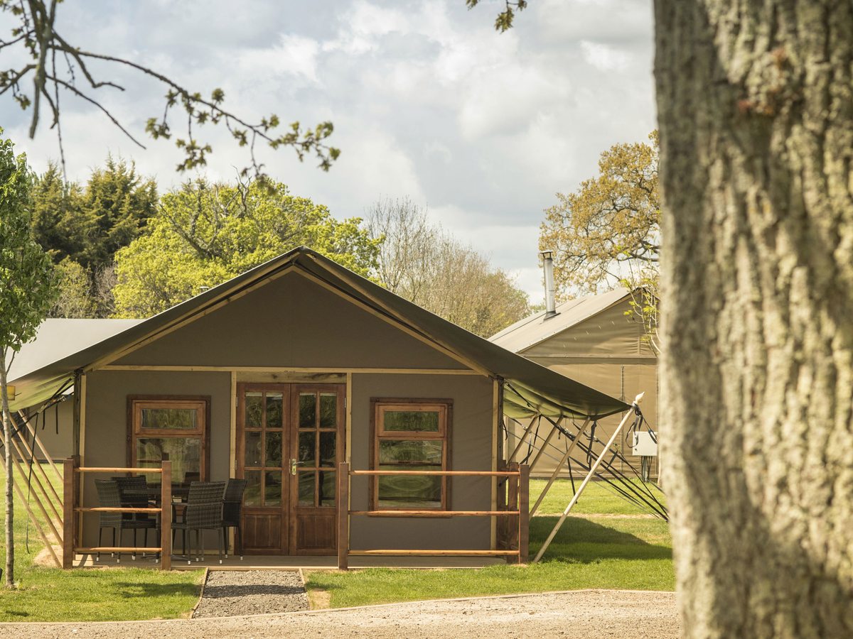 A safari-style glamping cabin with a pitched canvas roof, timber-framed doors and a small decked porch among trees