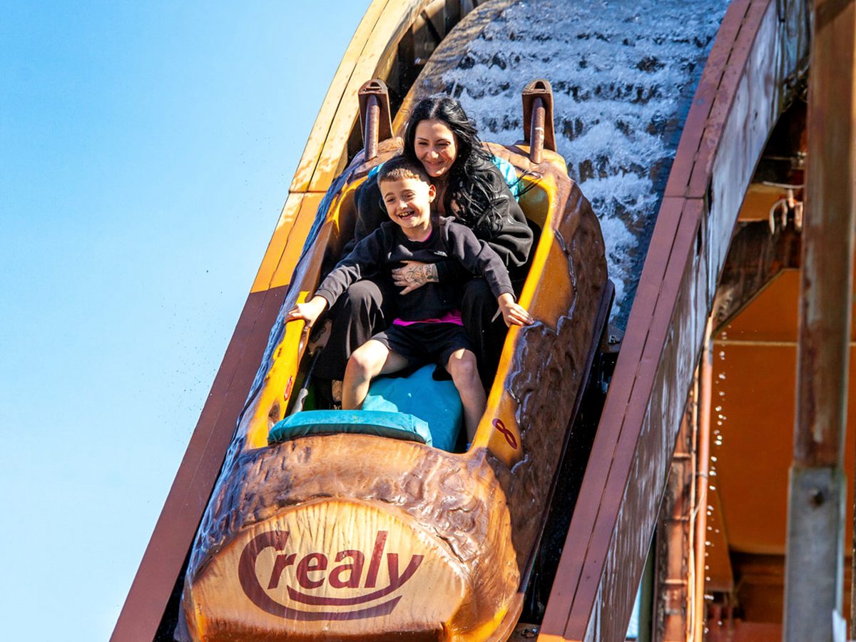 A mother and young boy smiling as their Crealy-branded log-flume boat comes down the water chute