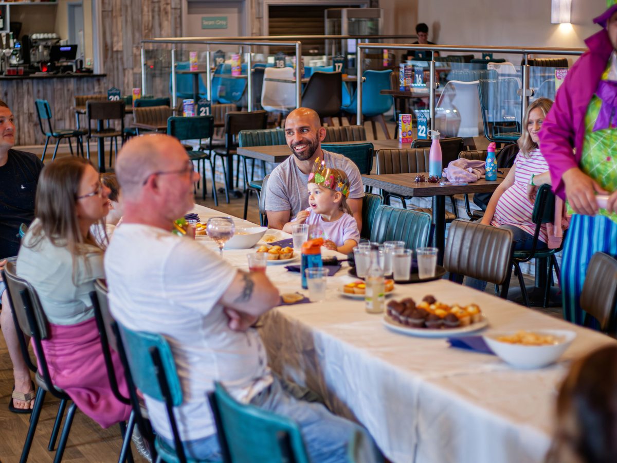 Families eating at long tables in the Clubhouse, with numbered tables and a bar counter behind
