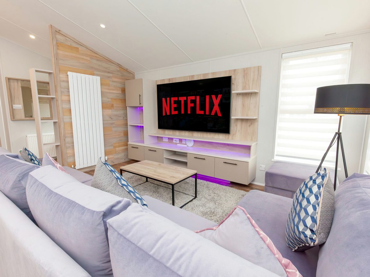 A lodge living room with a large wall-mounted TV showing the Netflix logo, purple accent lighting and lilac sofas