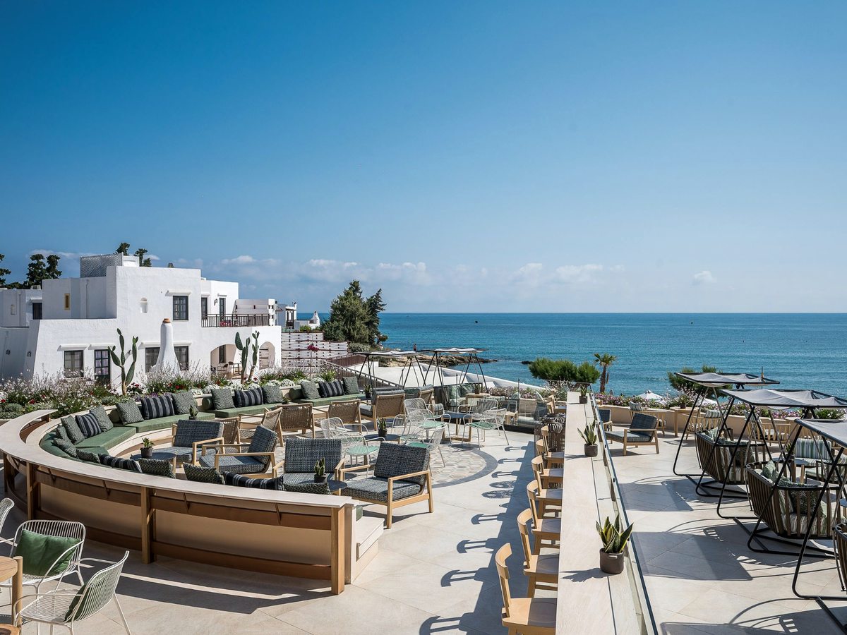A curved terrace bar with cushioned banquette seating and swing chairs on a whitewashed deck overlooking the open sea