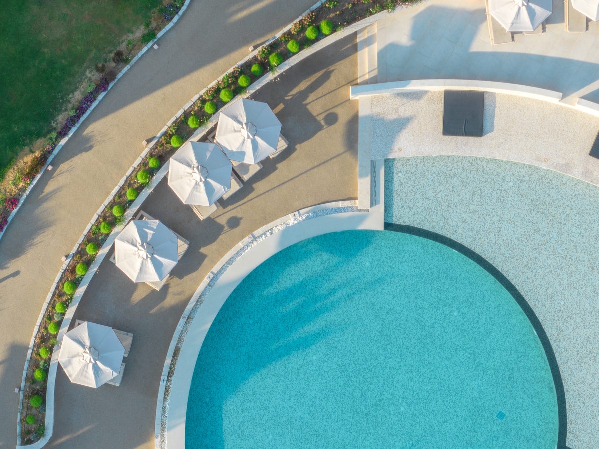 Aerial view of a curved freshwater pool edged by white umbrellas, clipped shrubs and a lawn