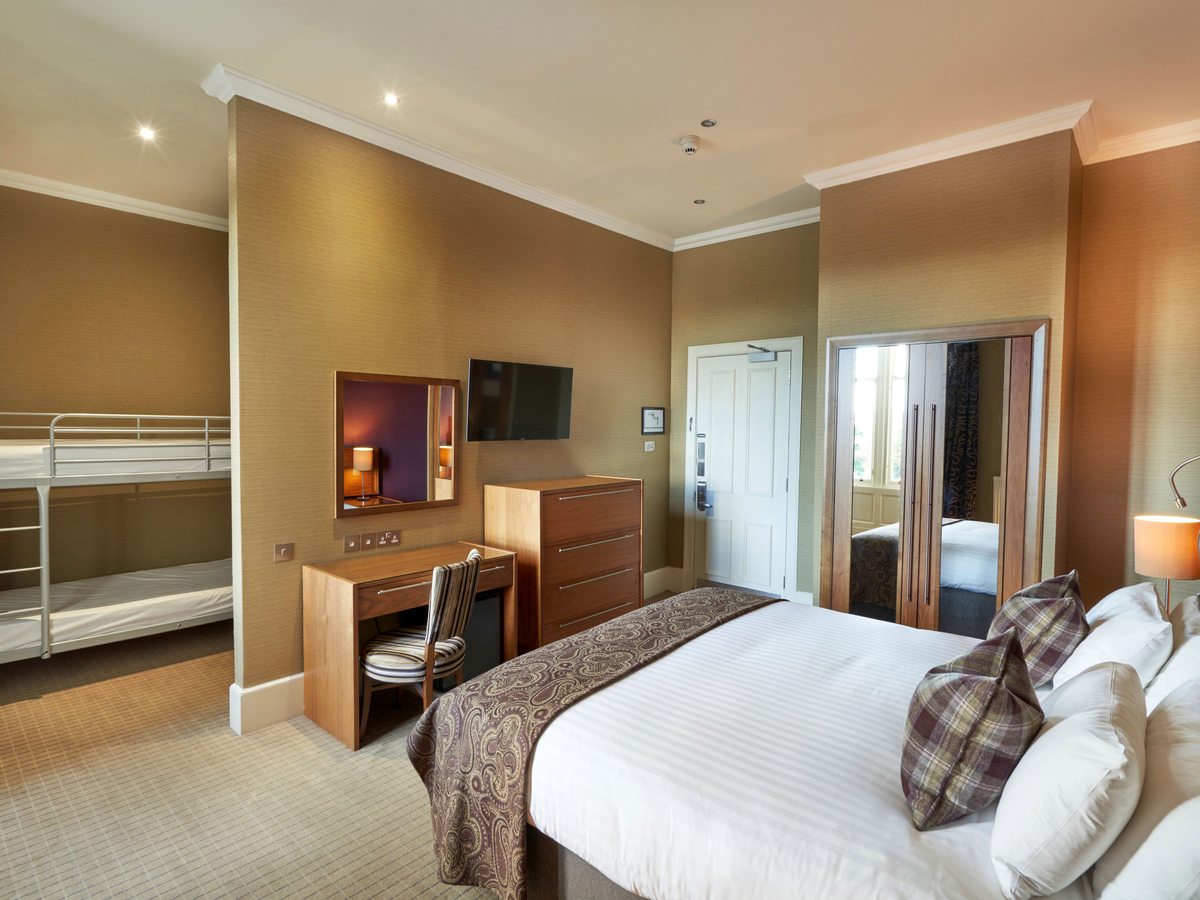 A family bedroom with a double bed, a set of metal bunk beds to one side and a doorway through to a further sleeping area.