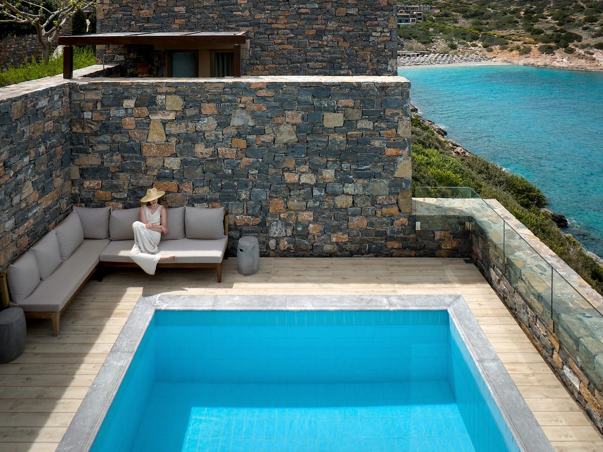 A small private pool on a timber terrace with a built-in corner sofa and a glass balustrade above the cove.