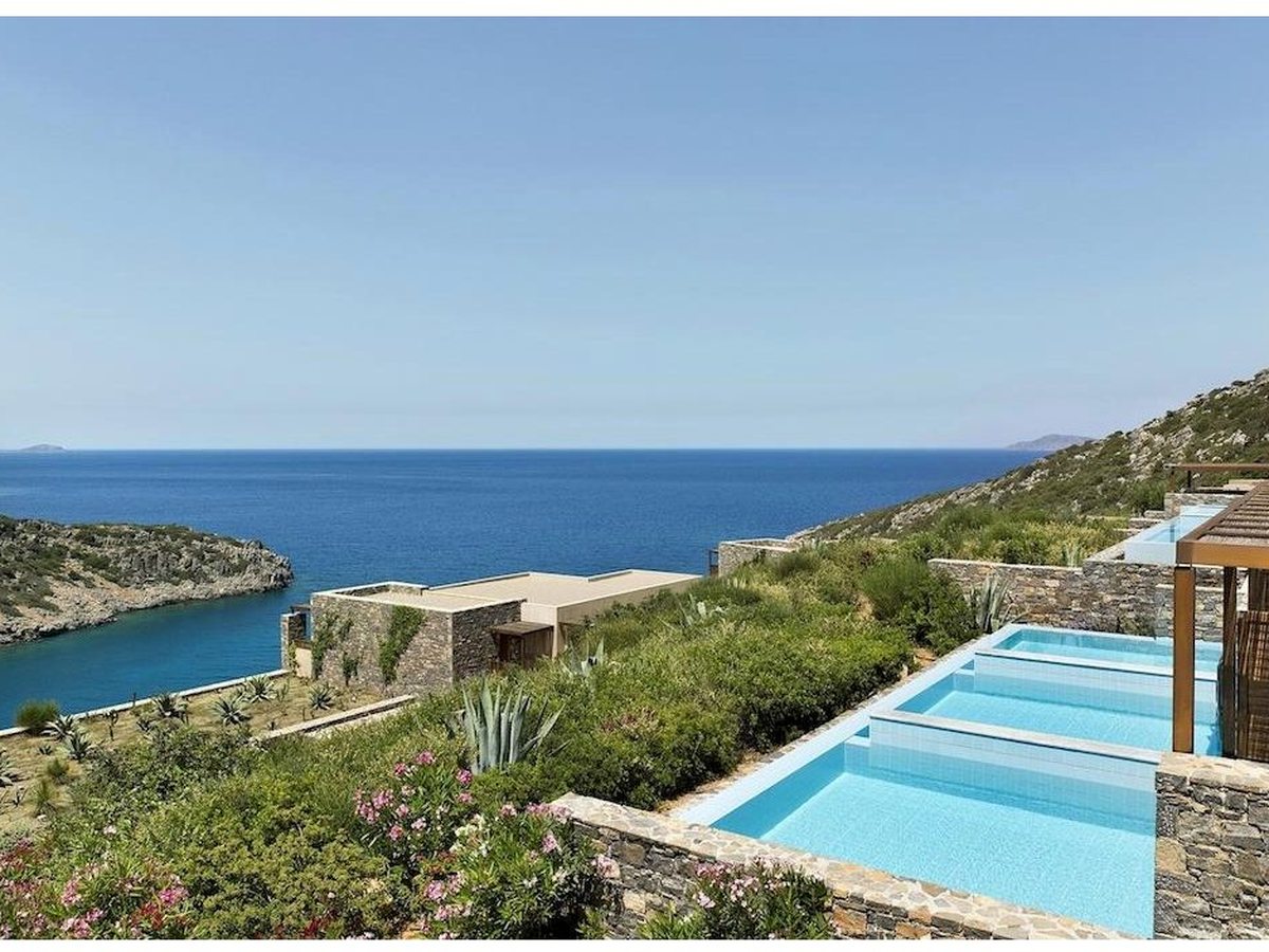 Stone villas set into the landscaped hillside, each with a private plunge pool and sea-view terrace above the cove.