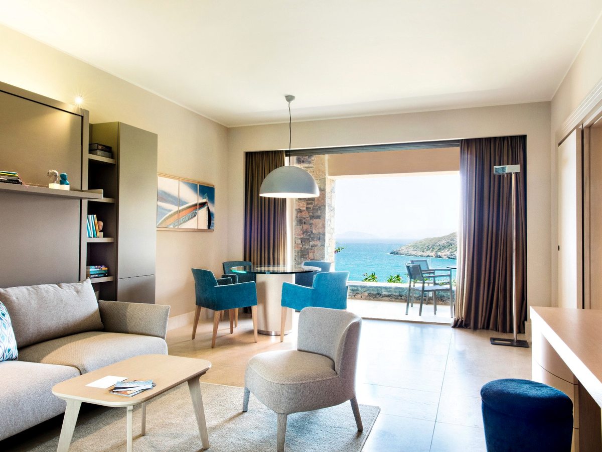 An open-plan suite lounge with sofas, armchairs, a dining table and wide patio doors onto a sea-view terrace.