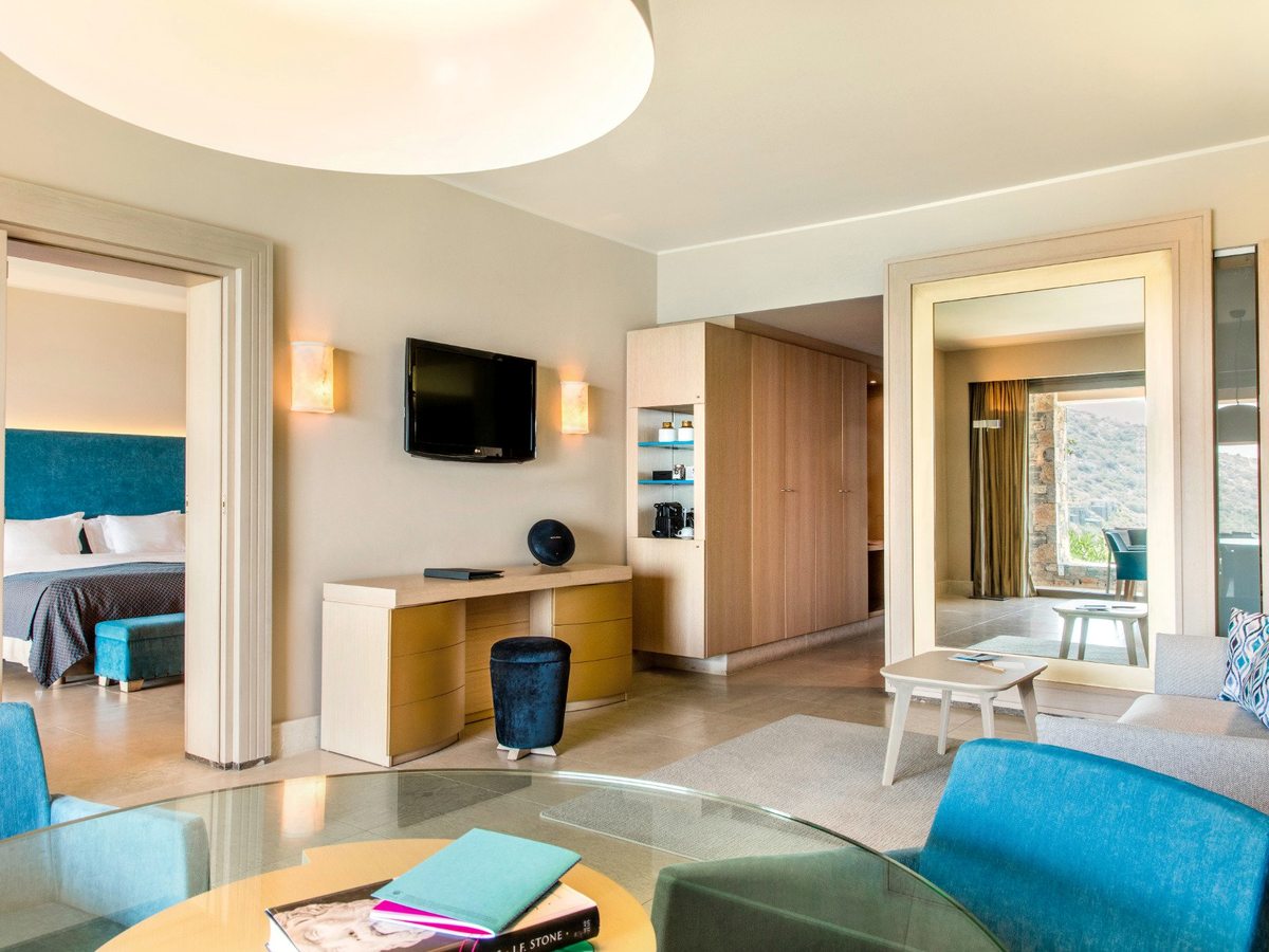 A suite living area with armchairs and a coffee table, its separate bedroom visible through open sliding doors.