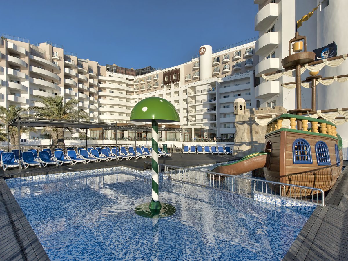A shallow mosaic-tiled splash pool with a green mushroom fountain, the pirate ship and the multi-storey hotel behind.