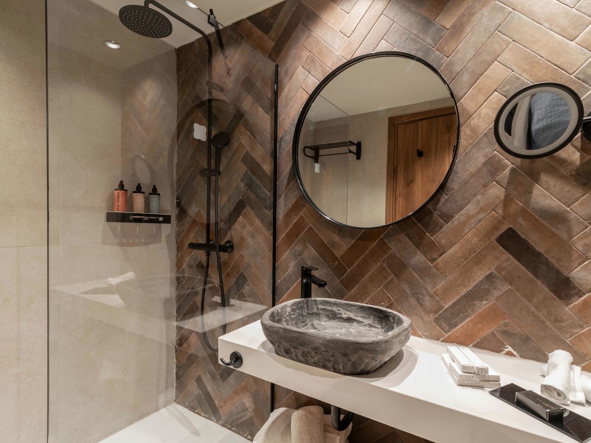 En-suite bathroom with a glass walk-in shower and rainfall head, a stone vessel basin, black tapware and herringbone tiling.