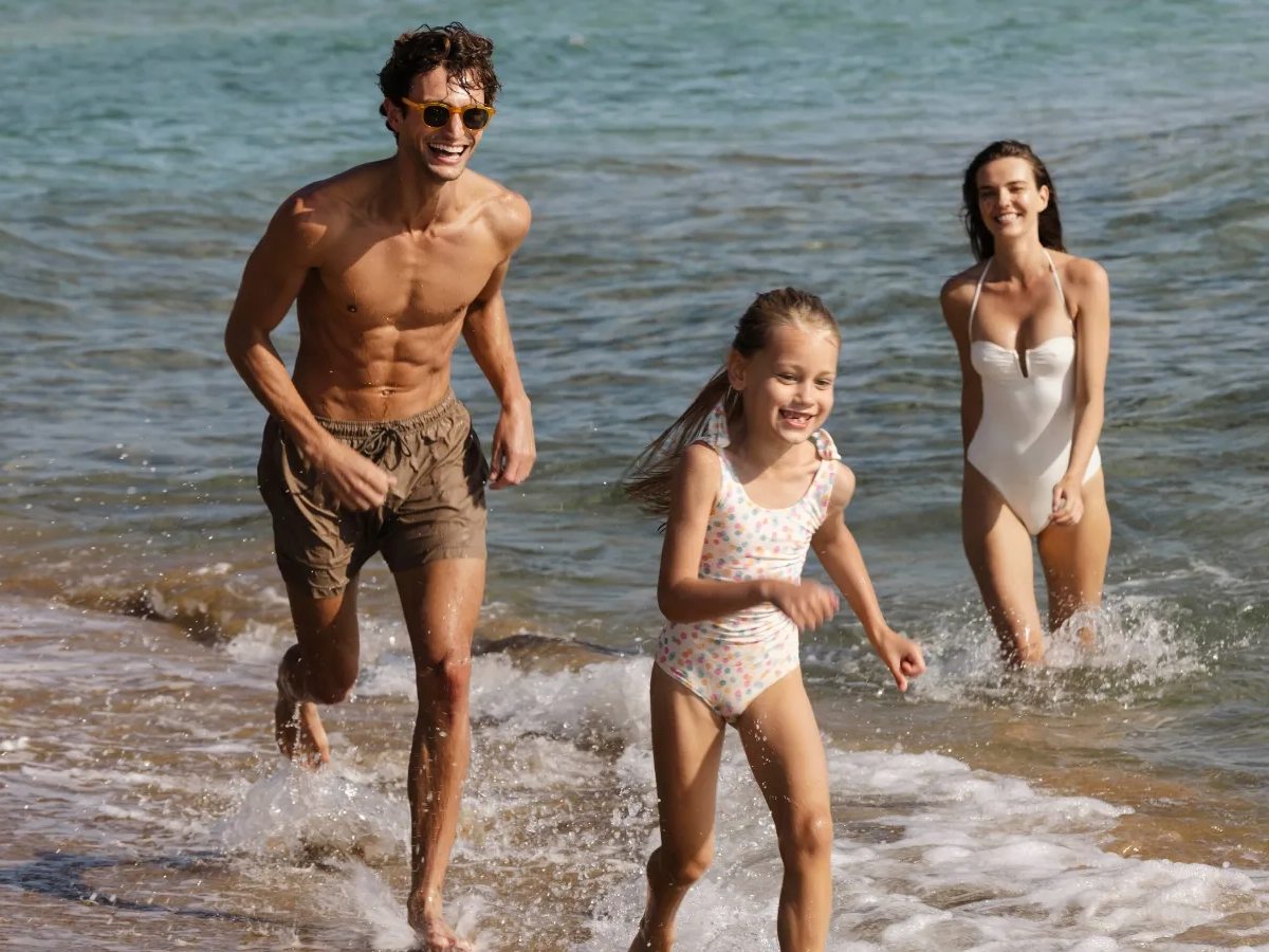 A man, a girl and a woman splashing through the shallow surf at the water's edge on a sunny day.