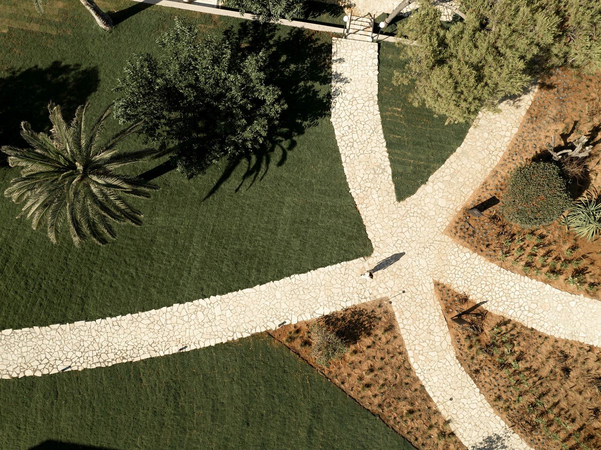 Aerial view of the resort's landscaped gardens with curving stone paths, manicured lawns, palms and mature trees between the buildings.