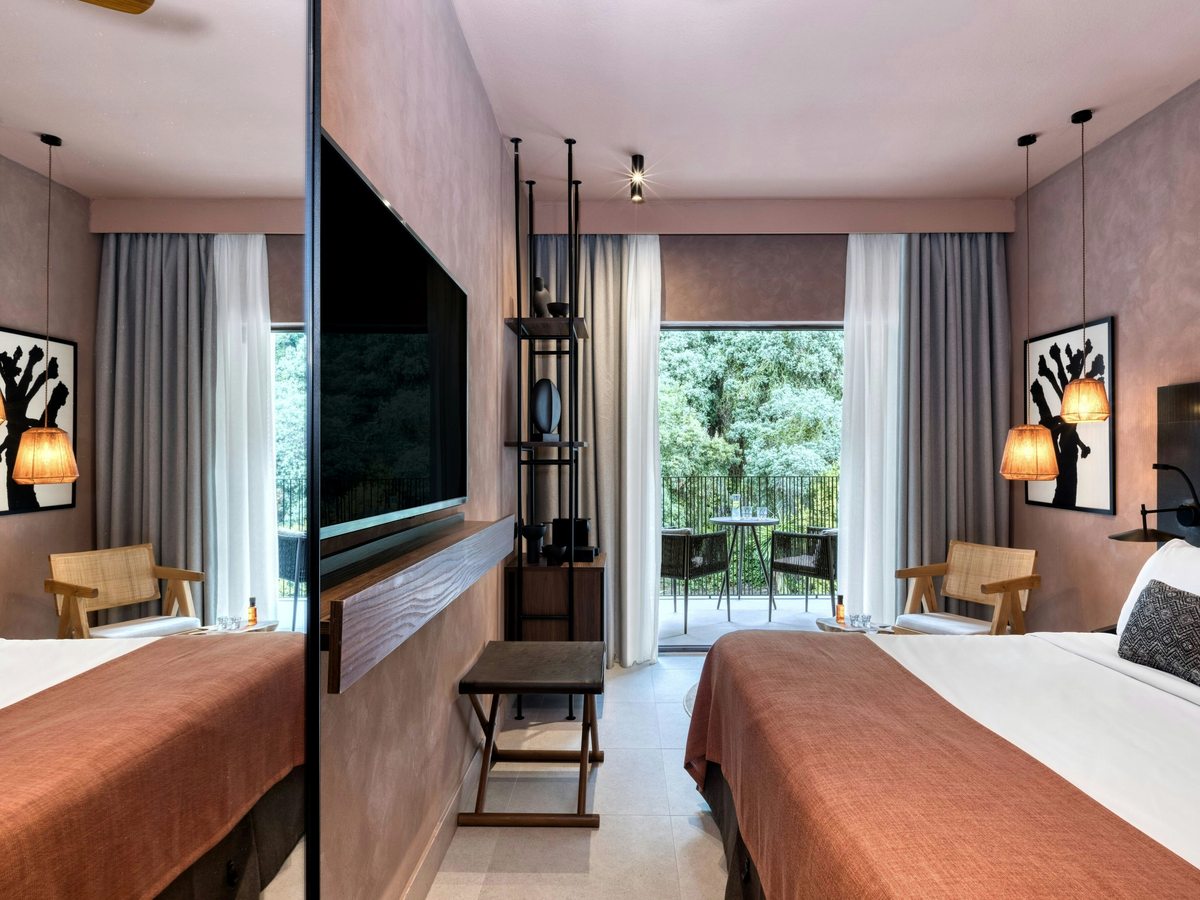 Family room with two separate beds either side of a central divider, each with its own television and reading lights, and doors onto a furnished balcony.