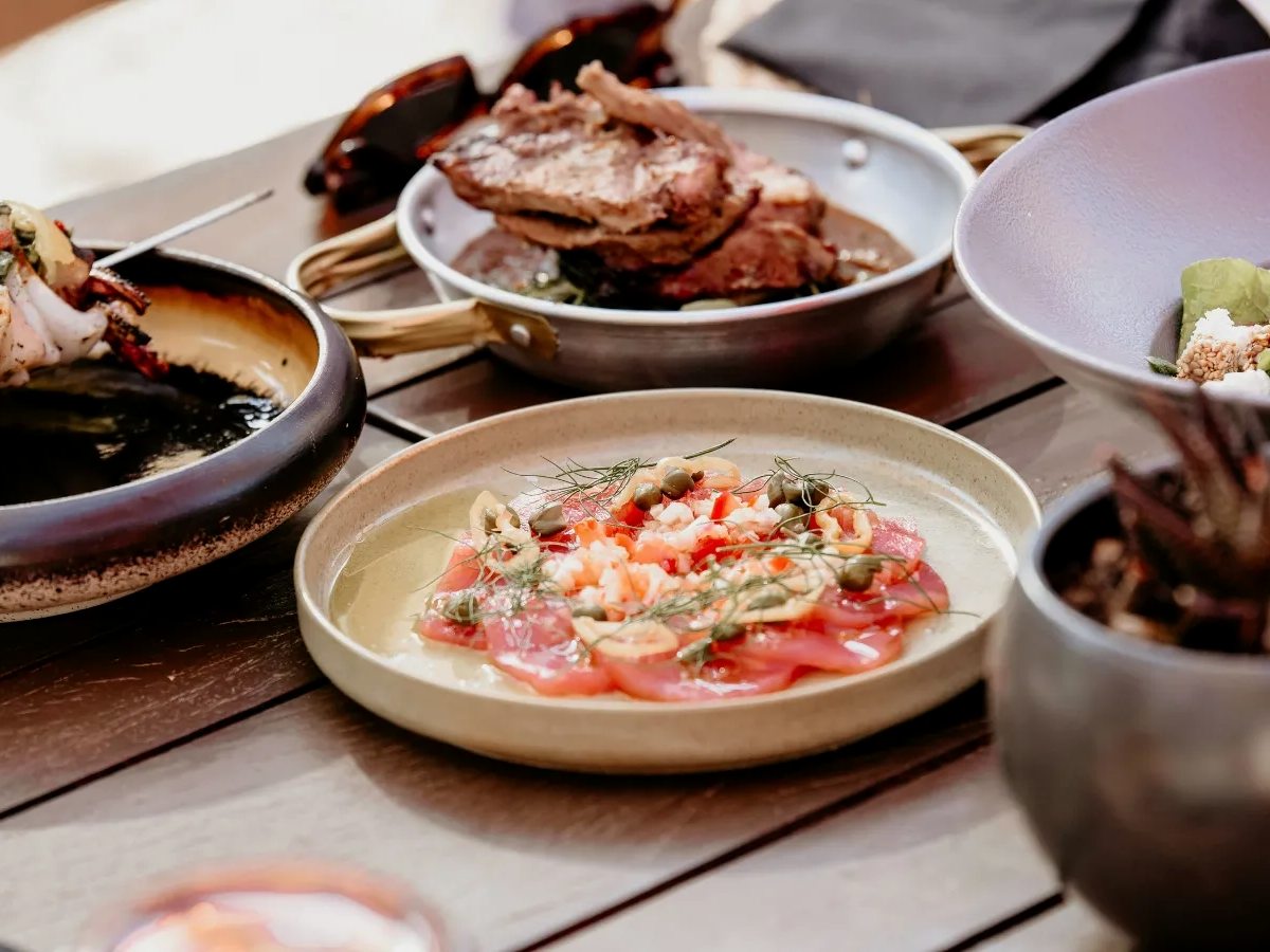 Sharing plates of fish carpaccio, shellfish and salads on a dark wooden table.