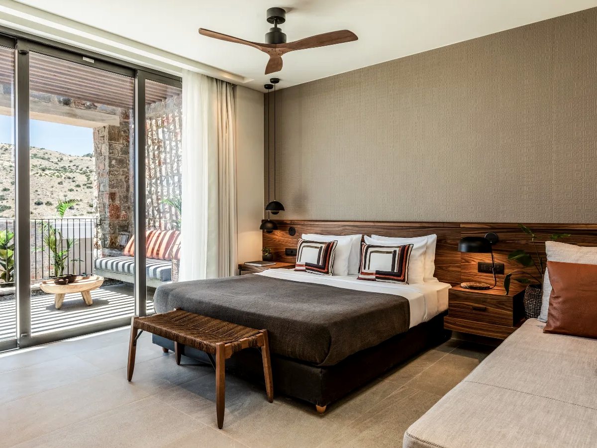 A double bedroom with a walnut headboard and sliding doors onto a balcony with a striped bench and a hillside view.