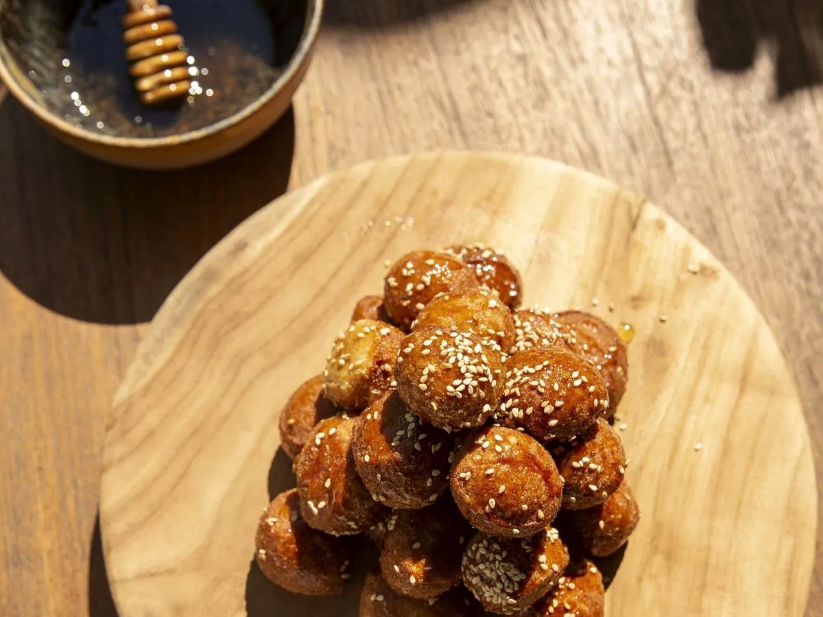 A wooden board of small honey-glazed fried dough balls dusted with sesame.