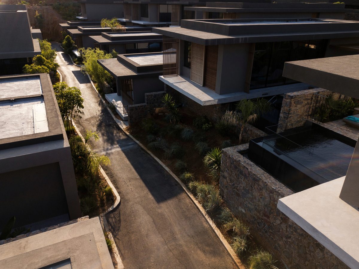 An aerial view of flat-roofed stone and concrete units stepping down a slope, each with its own walled terrace and plunge pool, linked by a narrow lane.