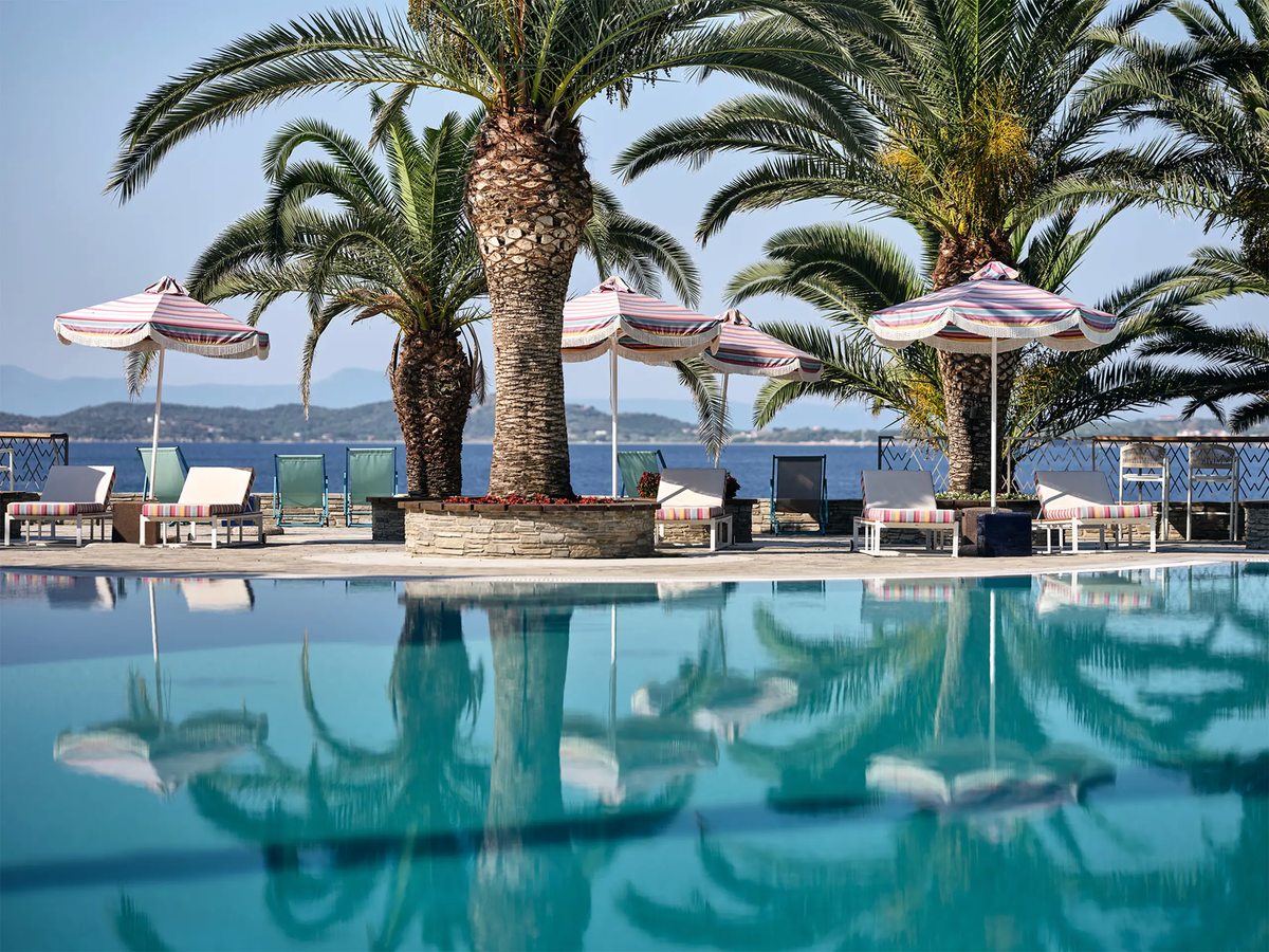 Freshwater outdoor pool ringed by sun loungers and striped umbrellas, with tall palms and a sea view beyond.