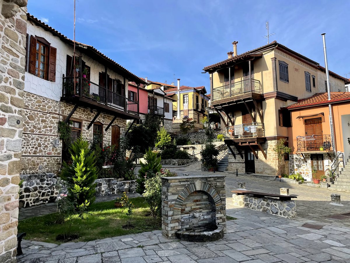 Stone-paved village square with historic houses, wooden balconies and shuttered windows.