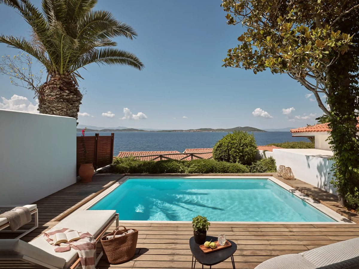 Private plunge pool on a wooden sun deck with loungers, framed by a palm and looking out over the sea.