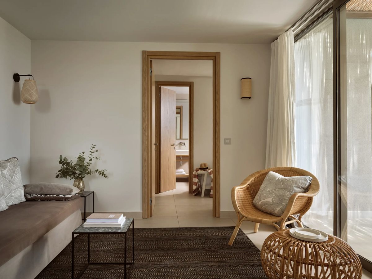 Bright suite sitting room with a low sofa and daybed, a coffee table and a woven chair, opening to a sea view.