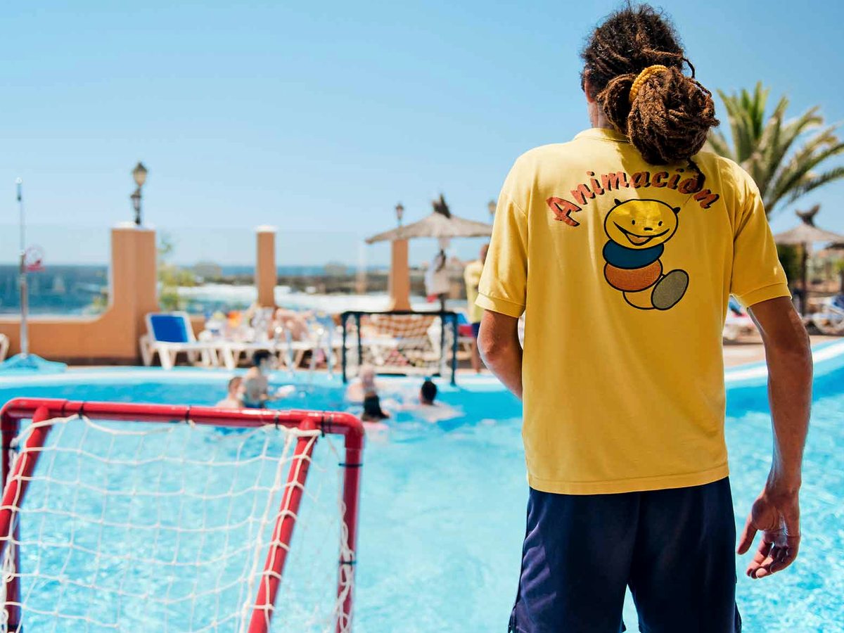A member of the animation team beside a water polo goal in an outdoor pool, with the sea in the background.