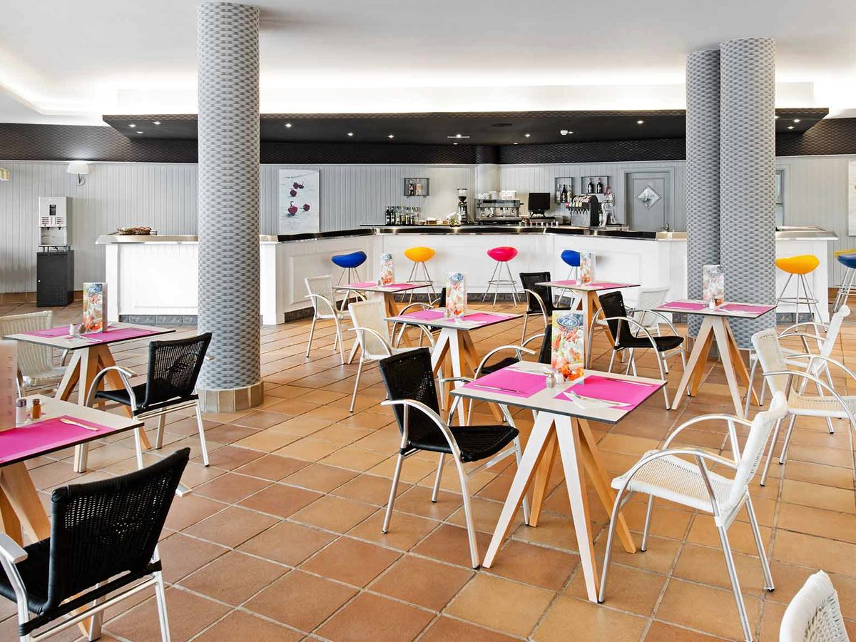 The poolside snack bar, an indoor cafe area with a white service counter, colourful stools and pink-set tables.