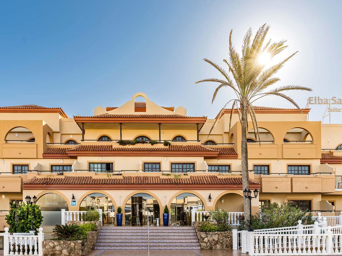 The resort's main entrance, a cream Spanish-style building with a terracotta tiled roof, arched balconies and a tall palm beside the entrance steps.