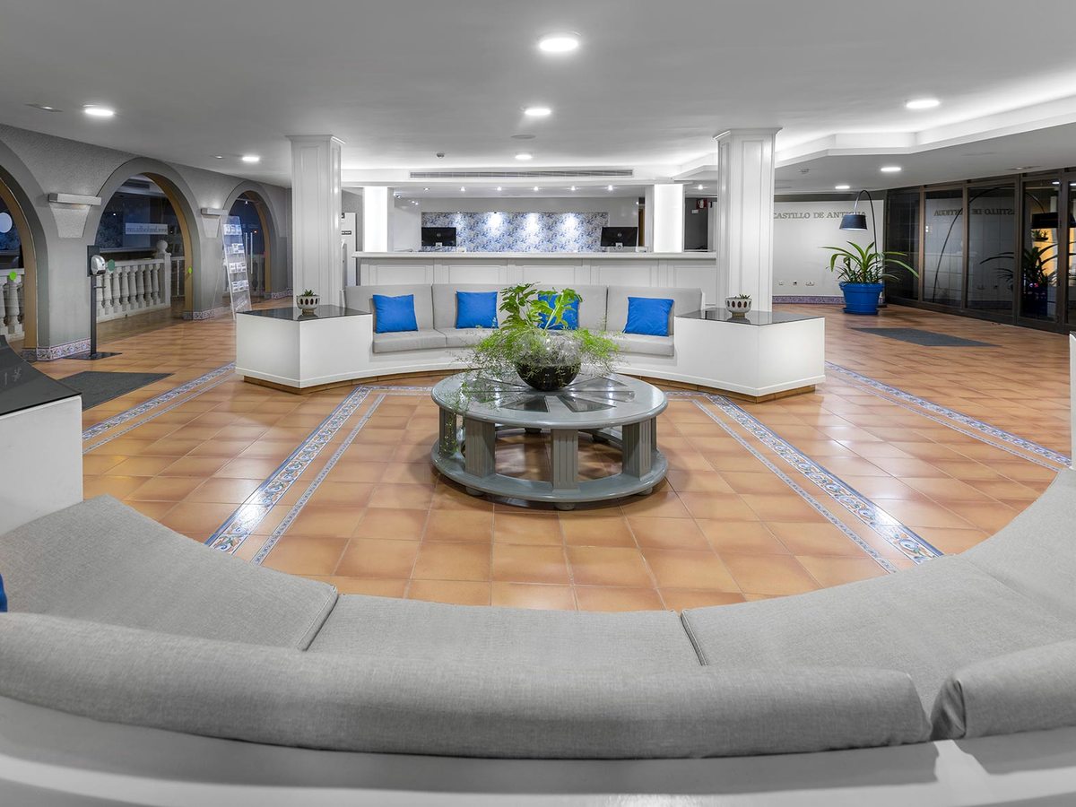 The reception lobby with a curved grey sofa, a white front desk under arched openings and a terracotta-tiled floor.