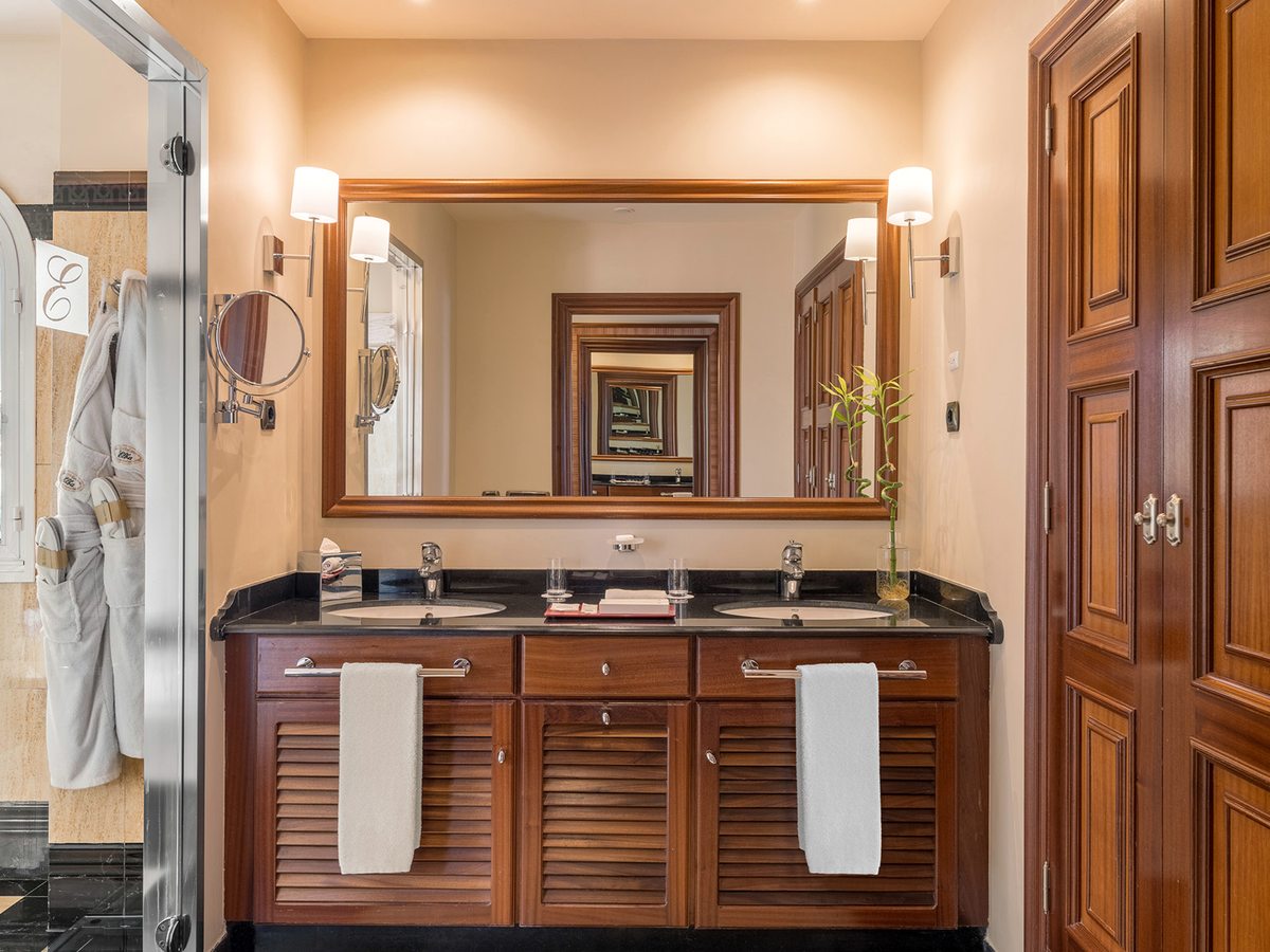 A bathroom with twin basins set in a black stone counter, wood cabinetry, a large mirror, bathrobes and a glass walk-in shower.