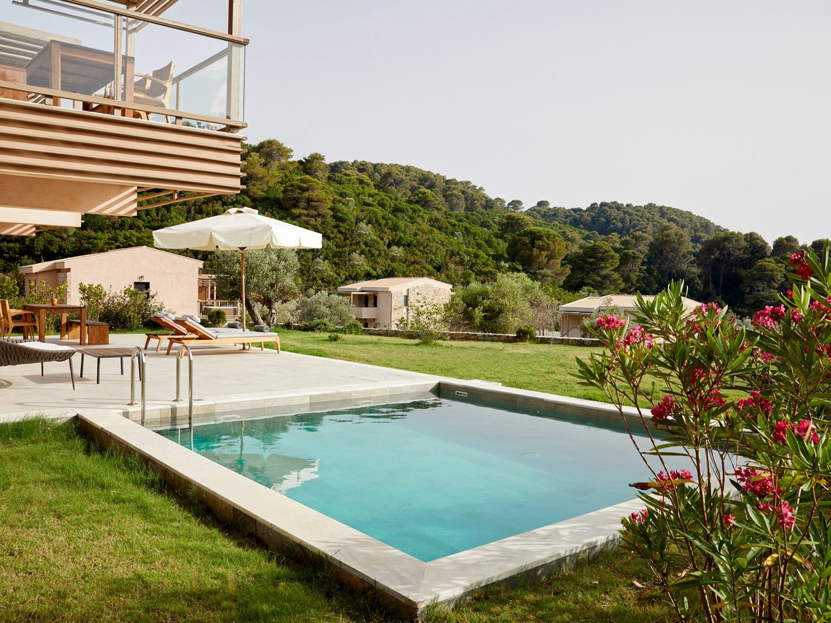 A rectangular private pool on a lawn edged with pink oleander, a parasol and loungers beside it and the sea beyond.