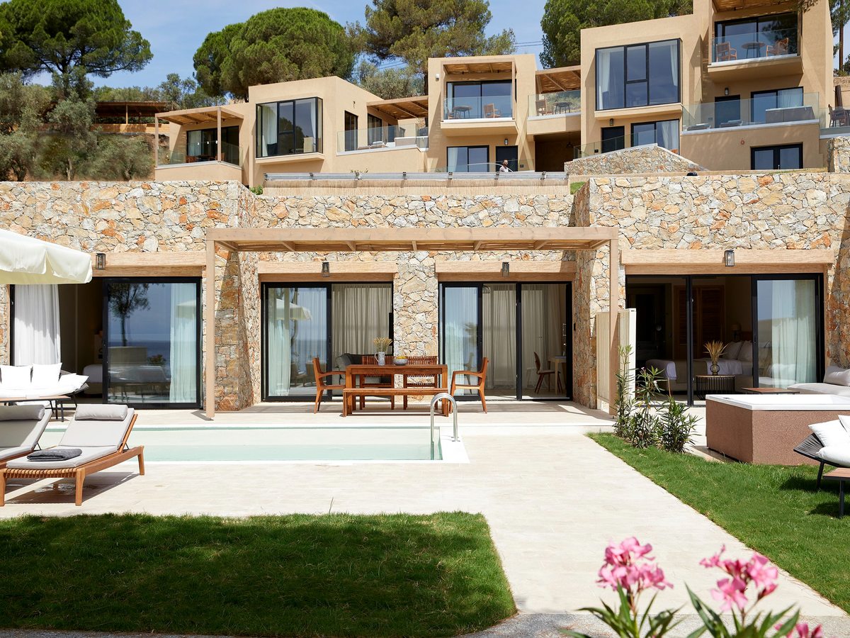 A single-storey stone-and-timber suite building with a small private pool, sun loungers and a lawn edged with pink oleander.