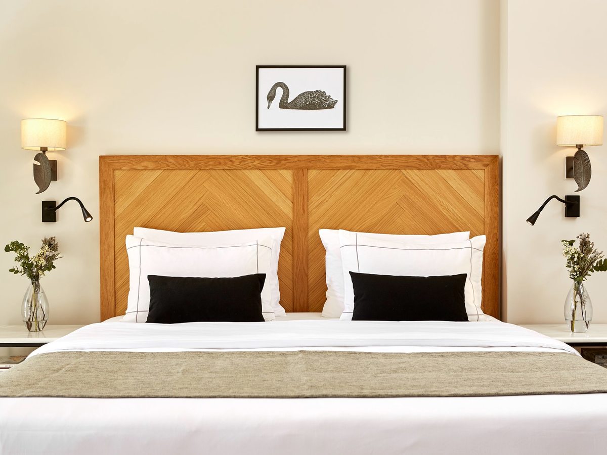 A double bed with a wooden chevron headboard and black-and-white patterned cushions, framed by wall lights and a framed swan print above.