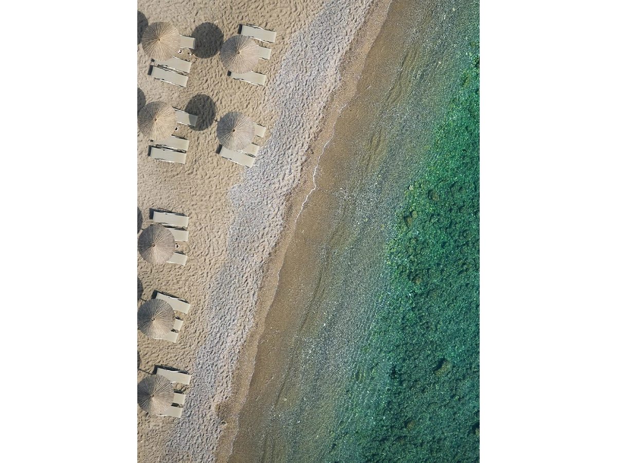 Rows of free sunbeds and umbrellas on the resort's sand-and-pebble beach with the sea beyond