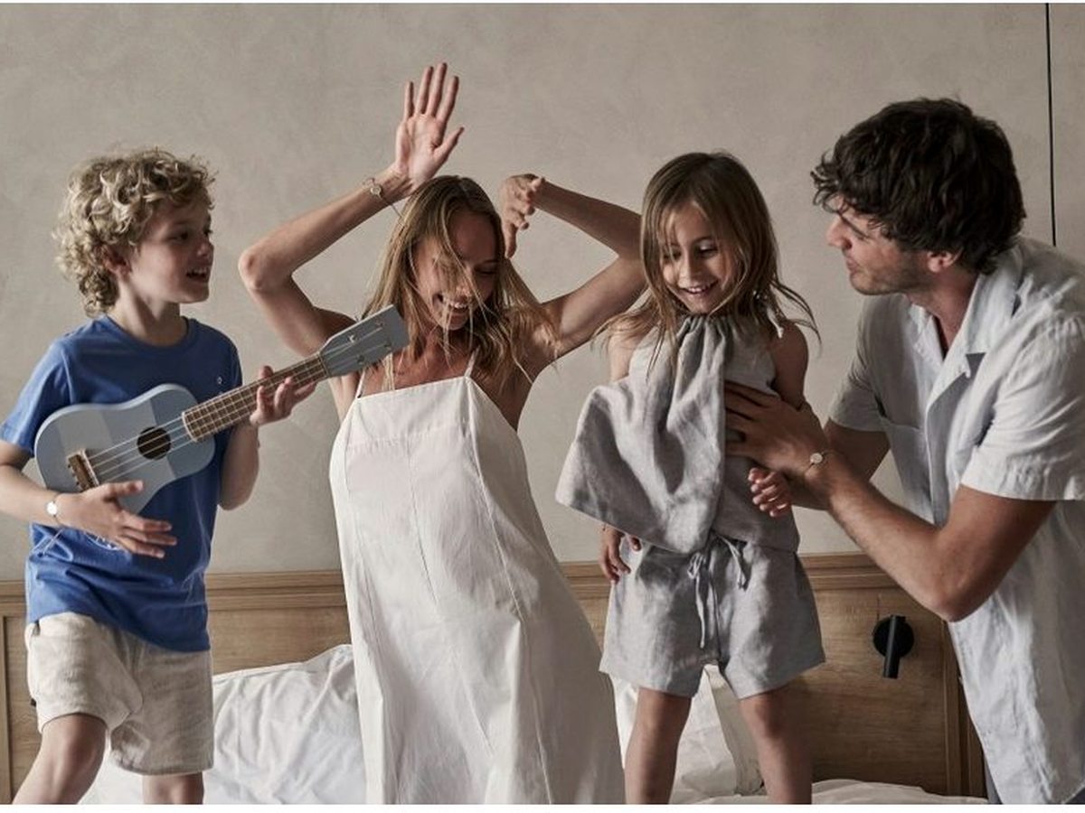 A family together on the bed in a guest room with a woven headboard and bedside lamps