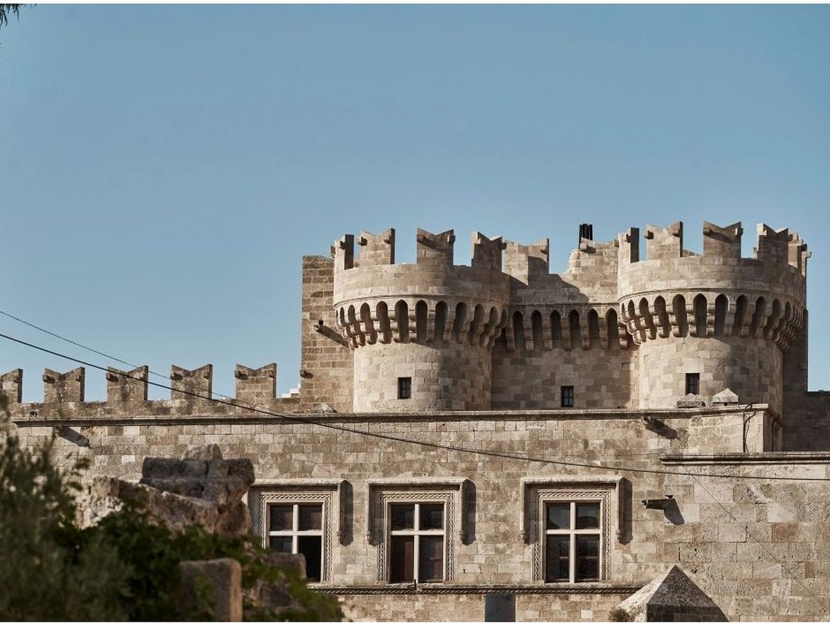 The crenellated stone walls and tower of a medieval fortress in Rhodes Old Town under a clear sky