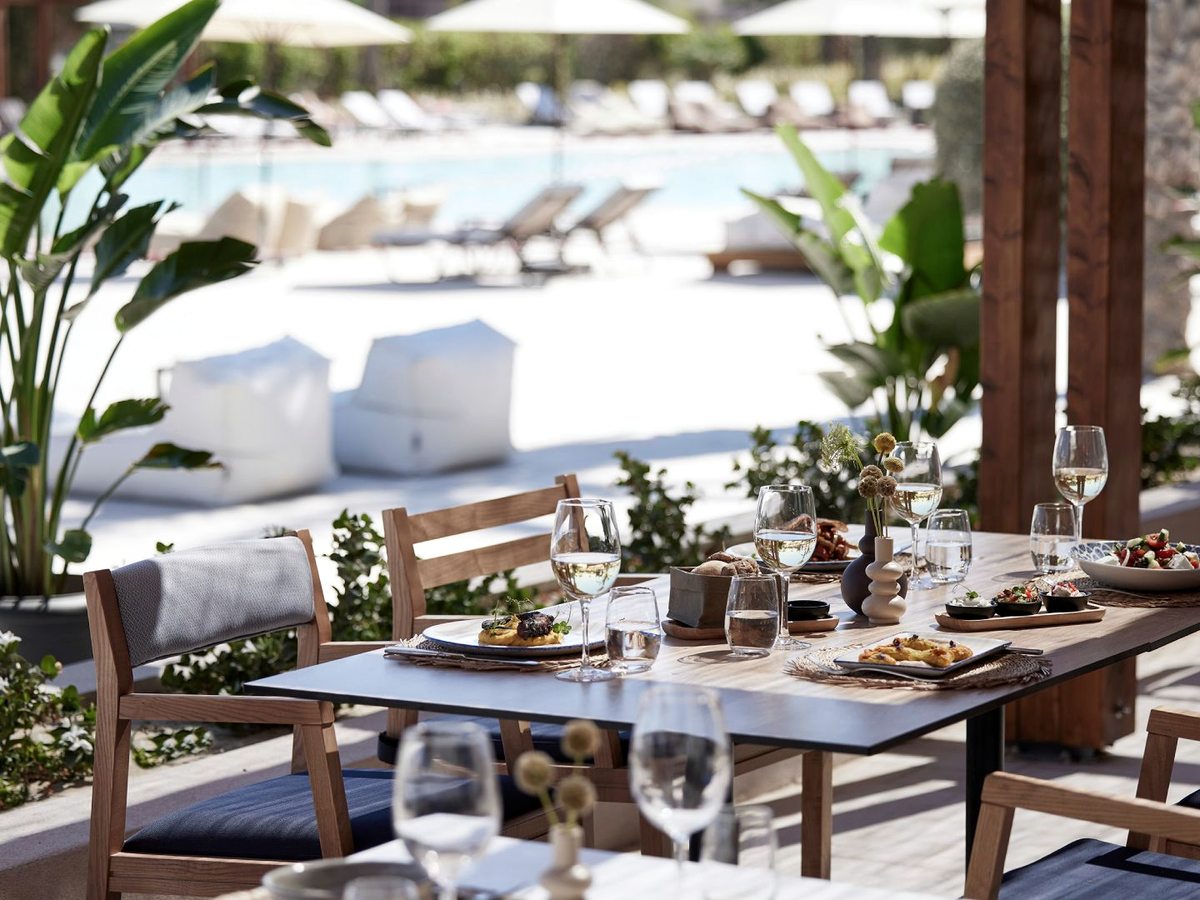 An outdoor restaurant terrace with white parasols and wooden tables set beside a swimming pool