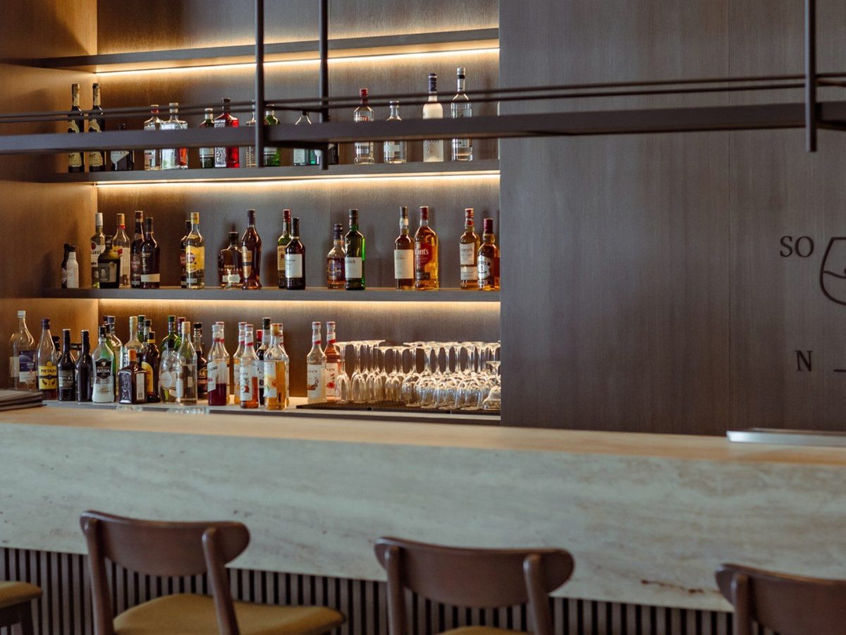 An indoor bar with a stone counter, leather stools and shelves of bottles behind