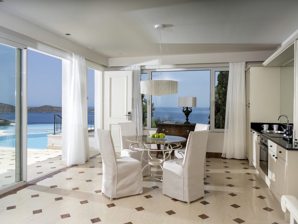 Open-plan villa kitchen and dining room with a round table, sliding glass doors to a private infinity pool and the gulf beyond.