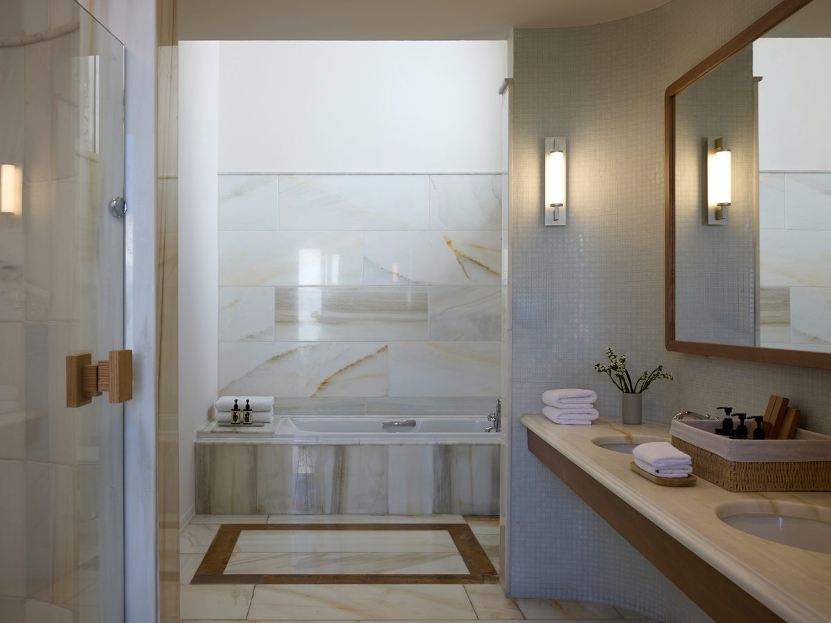 Marble bathroom with a walk-in glass shower, a built-in tub, twin basins on a stone vanity and a large mirror.