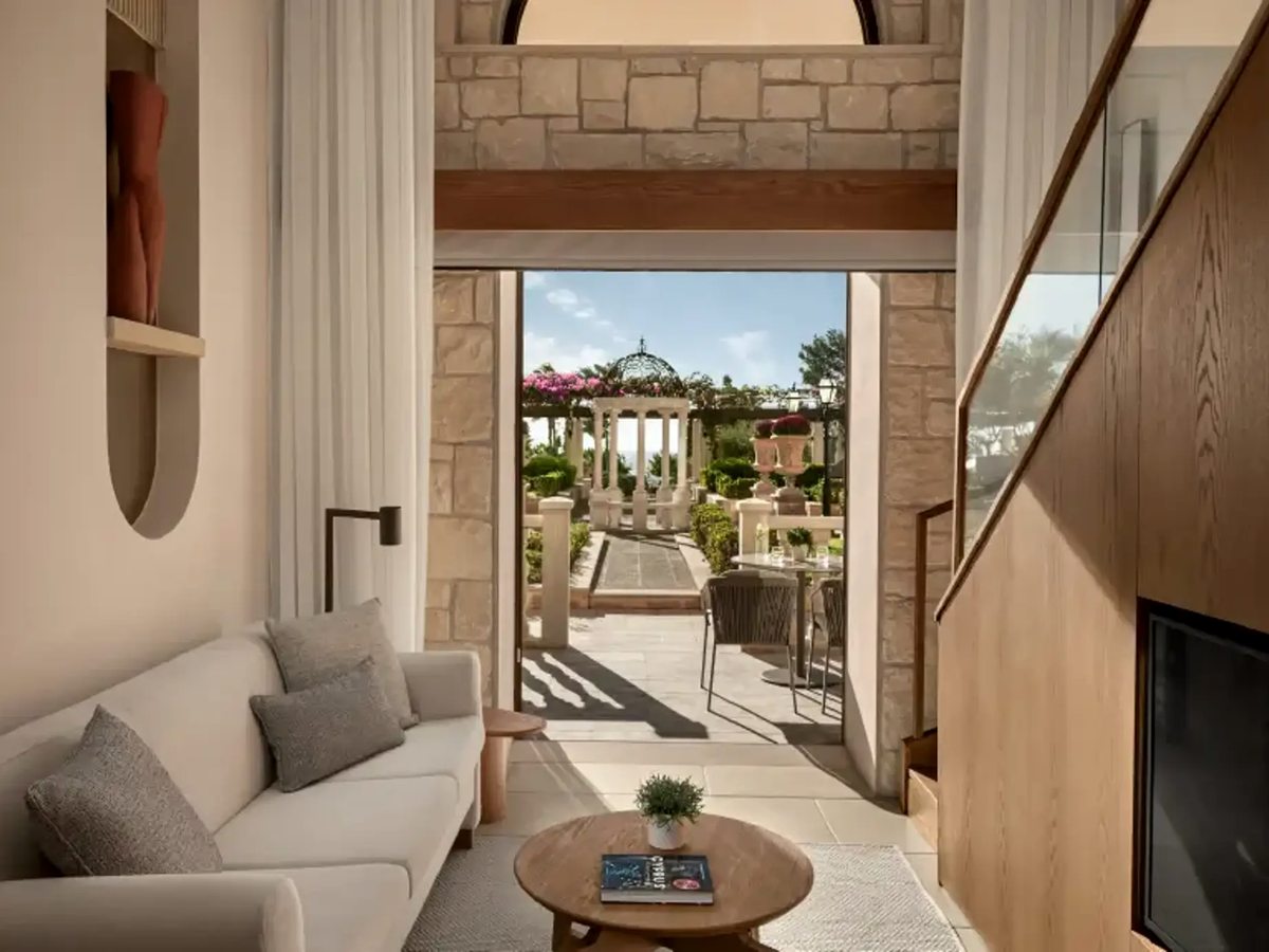 A suite sitting room with a pale sofa and round wooden coffee table, opening through wide doors to a garden terrace and gazebo.
