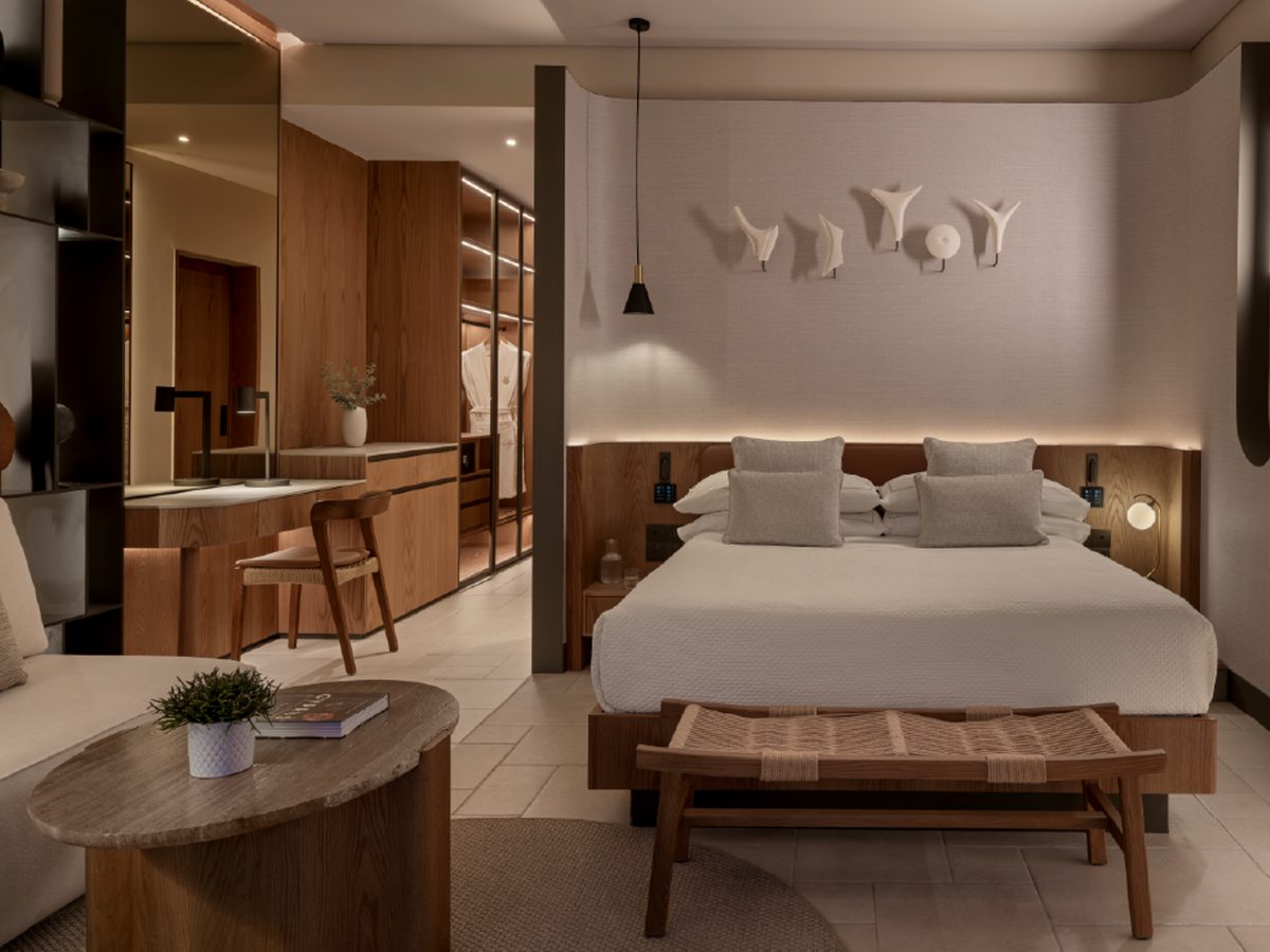 A contemporary room with a low bed, oak headboard and open dressing area in a calm, earthy palette.
