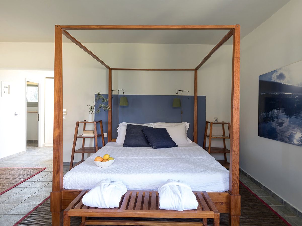A double room with a wooden four-poster canopy bed against a blue headboard, an open doorway to the bathroom beyond.