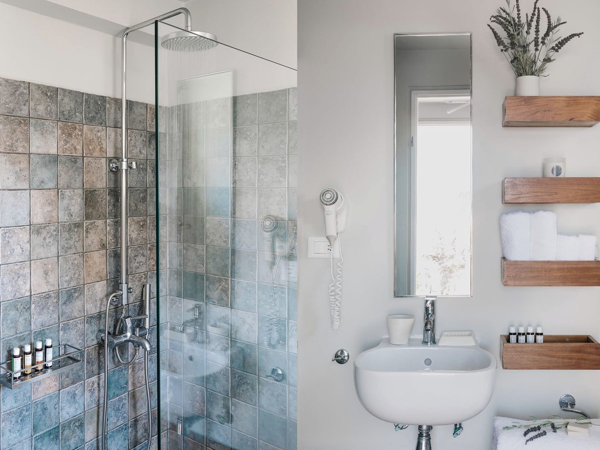A bathroom with a glass-screened walk-in shower, a wall-mounted basin, a mirror and folded towels on wooden shelves.