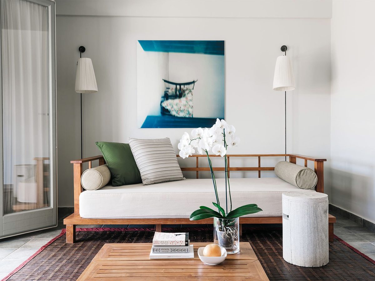 A suite sitting area with a wooden-framed daybed, cushions and a low table beside doors onto the terrace.