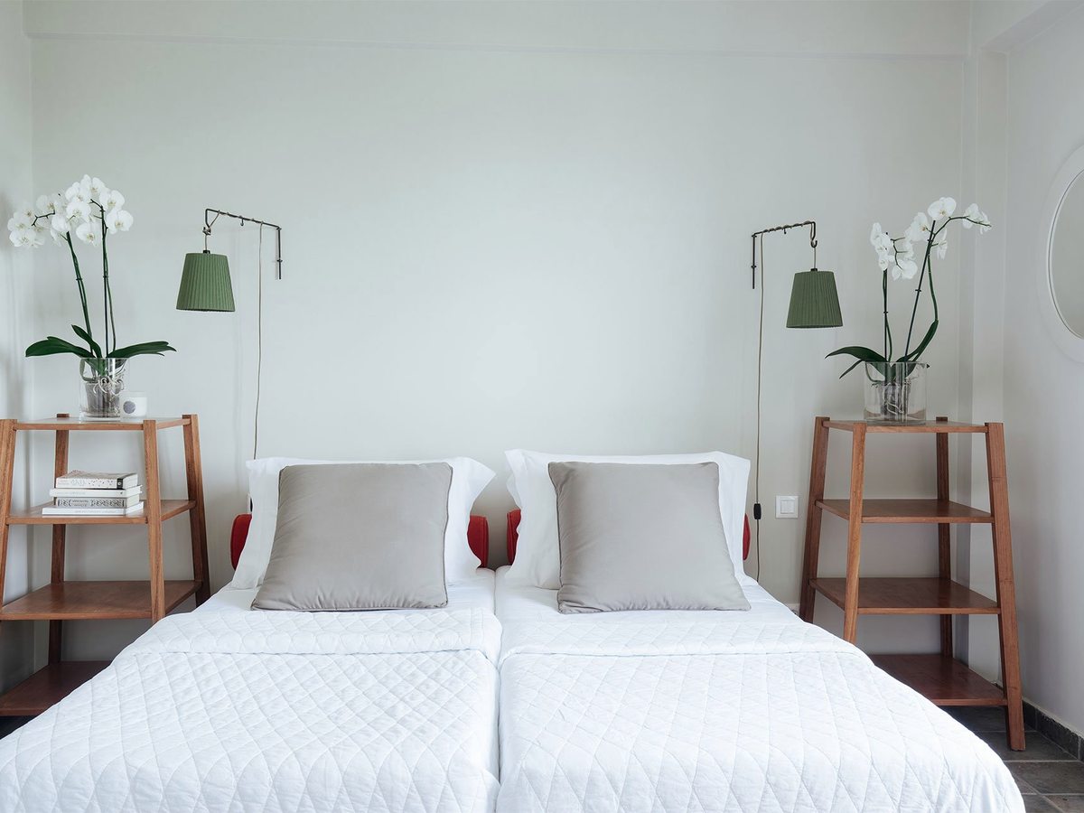 A room with two single beds made up side by side in white linen, orchids and reading lamps on either side.