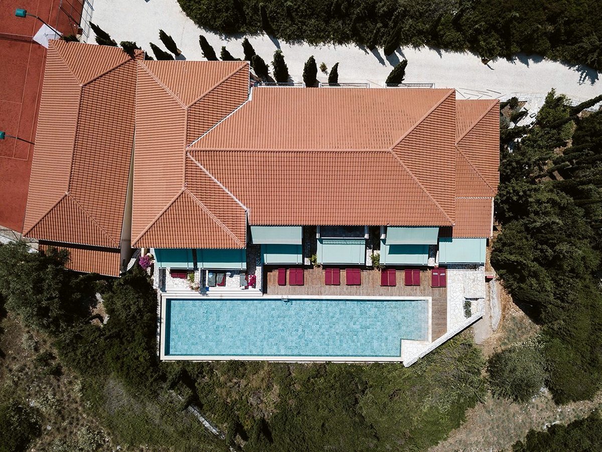 An aerial view of the resort's terracotta-roofed buildings on a wooded hillside, cypress trees and a tennis court alongside.