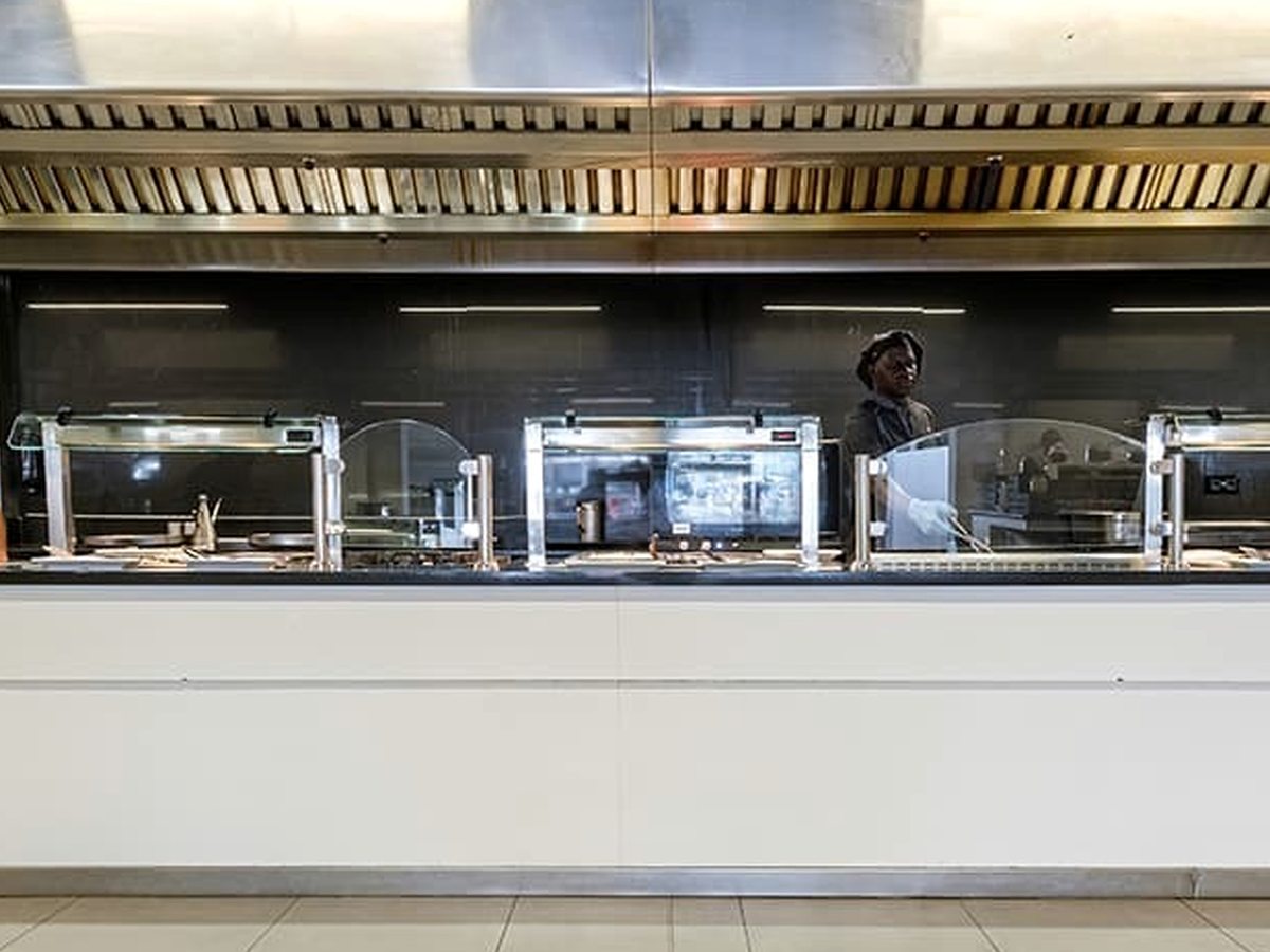A stainless-steel show-cooking counter at the buffet with heat lamps and a chef preparing food behind the glass.