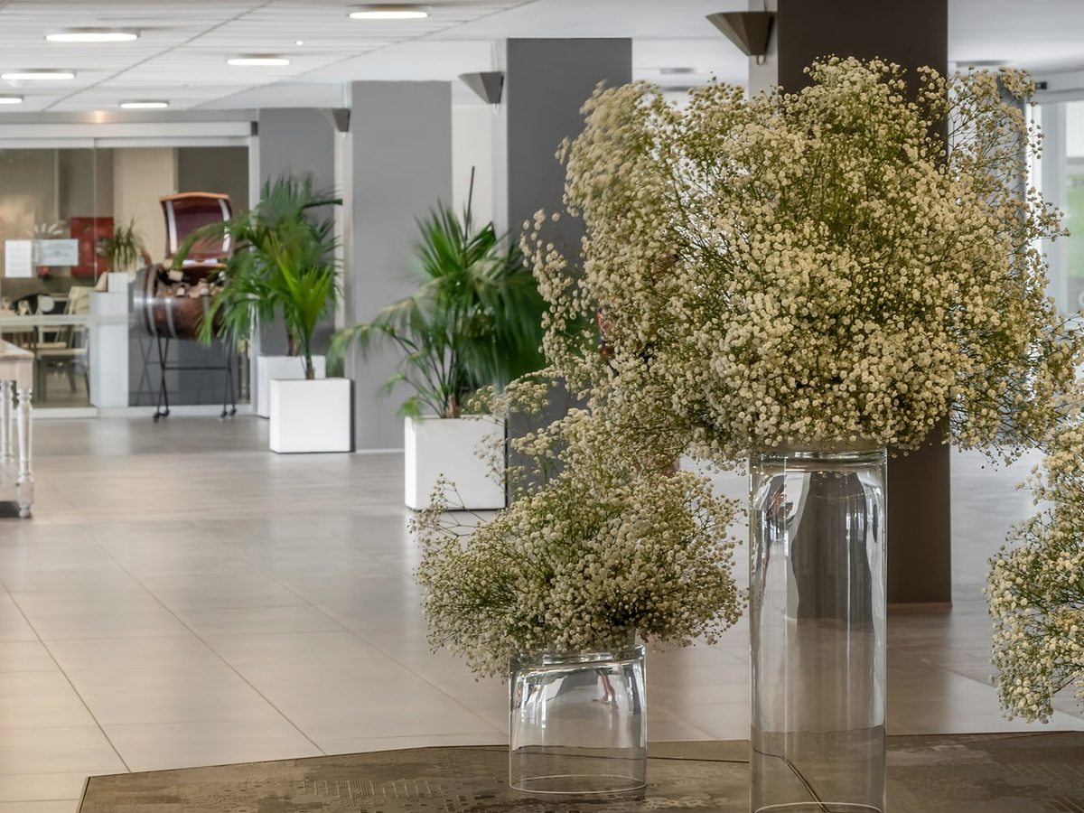 A bright tiled hotel lobby with tall glass vases of baby's-breath, potted palms and a reception area beyond.